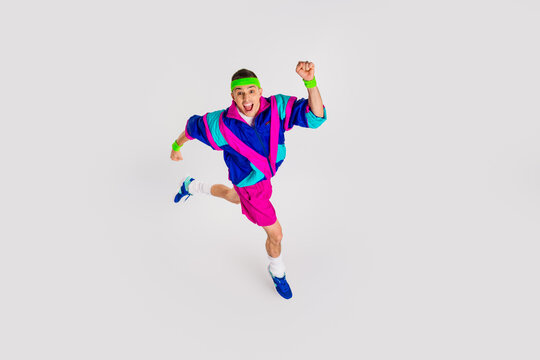 Energetic young man in vibrant retro sportswear jumping dynamically on a white background