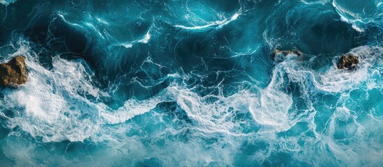 Obraz premium Turquoise ocean waves with white foam cresting against rocky shore creating a vibrant coastal scene with a serene blue ambiance.