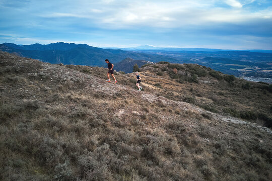 Aerial view of two hikers running uphill on a mountain trail with scenic landscape