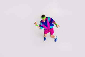 Young man in vibrant retro sportswear enjoying dynamic exercise on grey background