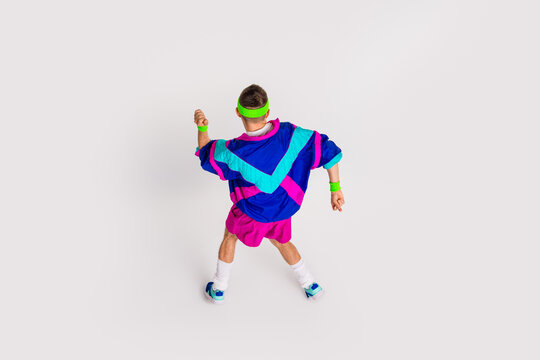 Energetic young man in colorful retro sportswear doing exercise on white background