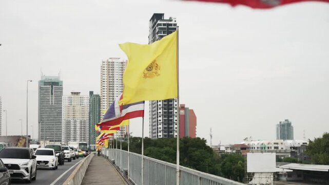Yellow royal flags and national flags of Thailand in a row waving in the wind on a King Taksin the Great Bridge on a cloudy day in Bangkok