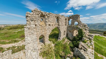 Wide panoramic view on old fortress in mountain landscape with lush green hills under clear blue sky, perfect for outdoor enthusiasts.