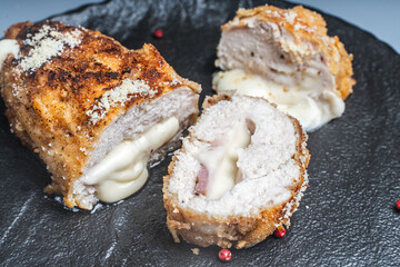 Cordon Bleu chicken cutlet with bacon and cheese on a black plate. Close-up