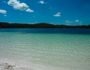 Pristine turquoise waters meet white sandy beach. Lake McKenzie, Fraser Island, Queensland, Australia. Crystal-clear freshwater lake surrounded by eucalyptus forest. Perfect tropical paradise scenery