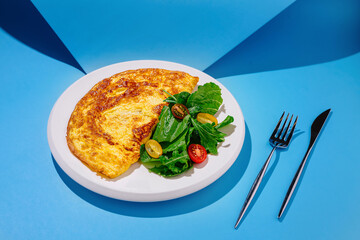 Delicious omelette served with fresh salad on a vibrant blue background during midday