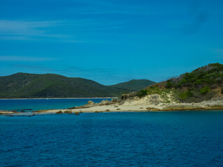 Pristine sandy beach with rocky outcrops stretches between turquoise waters and green hills at Great Keppel Island, Queensland. Tranquil bay with distant sailboats anchored near the shoreline