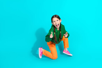 Playful young girl posing in colorful casual outfit on vibrant turquoise background