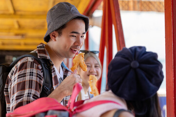 Young Asian man engaging in a lively conversation with friends while enjoying street food at a vibrant market, emphasizing travel and friendship.
