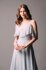 Attractive young lady in blue bardot evening dress. Sensual studio portrait of brunette woman. Bardot maxi gown with deep neckline, elegant look. Romantic bridesmaid's summer outfit