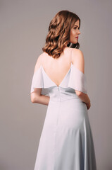 Gorgeous young lady in blue bardot evening dress, rear view. Sensual studio portrait of brunette...