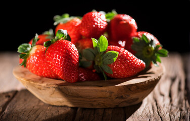 Strawberry, fresh ripe organic strawberries in a wooden bowl on a wood table over black background, close-up. Fresh ripe organic strawberries, macro shot of fresh juicy berries, close up. 