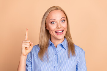 Smiling woman in blue striped shirt gesturing with raised index finger on beige background