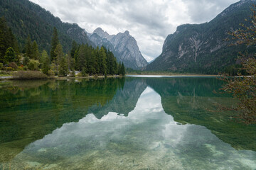 Lago di Dobbiaco, Italy – A breathtaking view of the crystal-clear waters of Lago di Dobbiaco reflecting the surrounding Dolomite mountains and lush pine forests. This picturesque alpine lake.