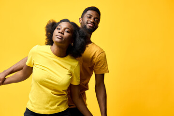Naklejka premium Young African American couple joyfully posing together on a yellow background, showcasing vibrant clothing and playful emotions