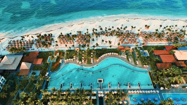 Aerial view of popular Caribbean sandy beach with sun loungers and umbrellas. Luxury resort with swimming pool along the beach. Flying drone view of luxury beach with beautiful sea in the background.