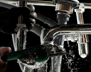Plumber used wrench to tighten loose nut on water drain pipe under kitchen sink. Hand glove hold...