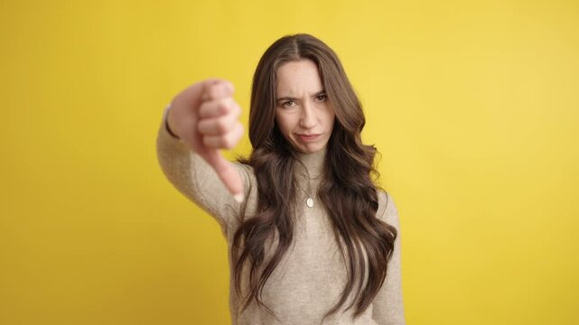 Young woman showing thumbs down on yellow background