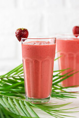 Strawberry cocktail, smoothie made of strawberries, coconut cream, green buckwheat with straws in glasses and palm leaves. Lactose and sugar free. Vertical orientation.