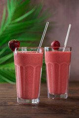 Glasses of strawberry milkshake, smoothie with palm leaves on brown background. Healthy food and drink concept. Lactose and sugar free. Vertical orientation.