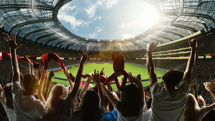 Fototapeta premium Emotional soccer fans. Enthusiastic supporters cheering with scarves and arms raised at massive stadium. Passion of the game. Concept of sport, emotions, competition, tournament.