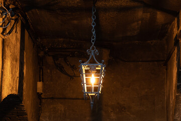 An antique lantern illuminates a narrow street in the Old Town of Nice, France. Shadows fall on the...