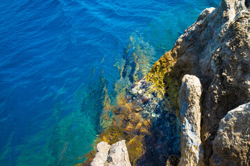 Rugged coastal rock formation meeting clear blue water of Mediterranean sea, where sunlight highlights contrast between deep water and textured shoreline