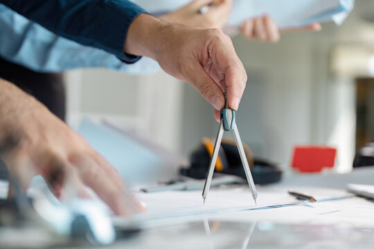 Architect using compass to design plans on a workspace table.