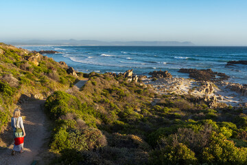 A Woman enjoying a stroll along the rugged, rocky coastline on the Cliff Path at Hermanus, Whale Coast, Overberg, Western Cape, South Africa. © Roger de la Harpe