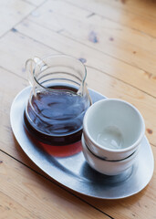 Glass server with black filter coffee inside and ceramic cup stand on wooden cafeteria table, day light from window. Making filtered coffee in coffee shop. Pour over method of alternative brewing, v60