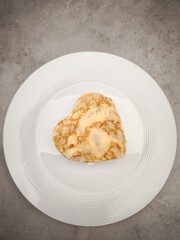 Delicate heart shaped crepes with yogurt folding elegantly over white plate, resting on textured gray surface for Mother's Day Valentines copy space