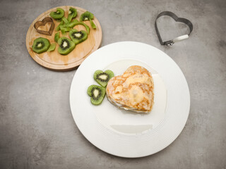 Heart shaped crepes, pancakes served on a white plate with kiwi slices, yogurt and honey, agave nectar, creating a romantic and delicious breakfast for Mother's Day Valentines copy space