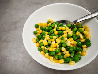 Ceramic bowl overflowing with bright green peas and yellow corn kernels, displaying fresh vegetable medley with nutritional value copy space Galentines day