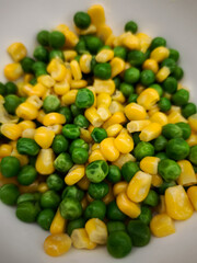 Green and yellow peas and corn kernels mixing together in pristine white ceramic bowl, highlighting fresh vegetable medley