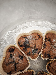Delicious heart shaped blueberry muffins freshly baked and sprinkled with icing sugar, resting on an elegant glass plate for Mother's Day Valentines copy space