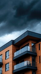 Fototapeta premium Modern apartment building with wooden facade under dramatic stormy sky in urban setting during late afternoon