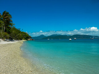 Pristine turquoise waters meet a secluded coral beach on Green Island, Great Barrier Reef. Luxury yachts anchored in crystal-clear bay against a backdrop of distant mountains in Queensland