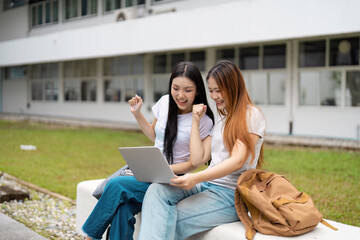 Excited diverse university students celebrating their academic success together while studying on campus with a laptop.