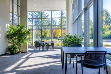 Modern office lobby with large windows, sunlight, plants, and tables with chairs.