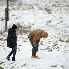 Two individuals, one adult and one child, enjoy a snowy day. The adult bends to shape a large...