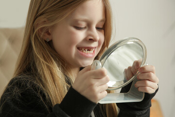 Cute 7 year old girl looking in the mirror her growing front teeth 