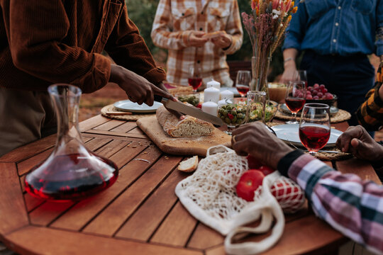 Person slicing bread at a convivial outdoor meal with friends