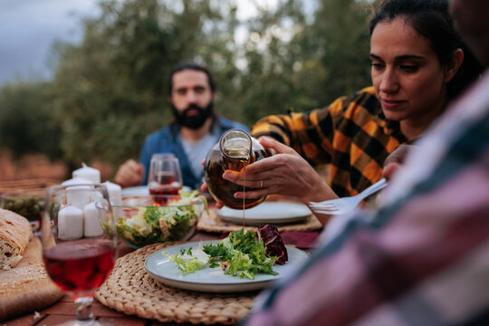 Woman pouring olive oil on salad during outdoor meal with friends - Powered by Adobe
