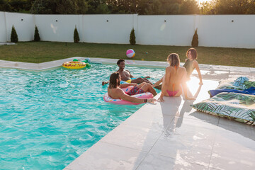 Friends enjoying summer holidays relaxing in swimming pool at sunset