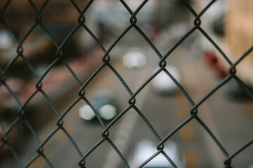 Fototapeta premium Blurred two lane city traffic behind chain wink wire mesh grid or fence. Top, overpass point of view, close up shot, no people