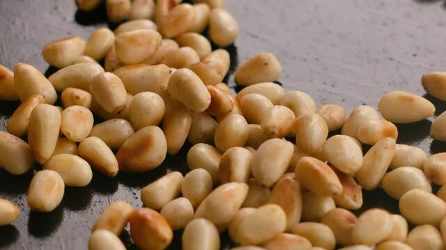 A spatula stirs browned pine nuts onto a frying surface close-up. High quality 4k footage