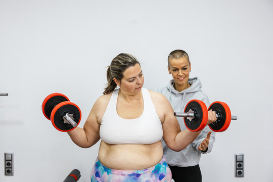 Personal trainer supporting client lifting weights in gym