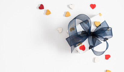 Holiday background with gift. Wonderful cute white gift with confetti hearts and beautiful tied bow from blue ribbon. Father's day, mother's day, valentine's day, birthday concept. Top view, Flat lay.