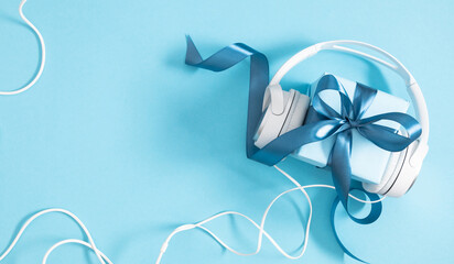Gift box with ribbon with headphones on a blue table background. Top view with copy space