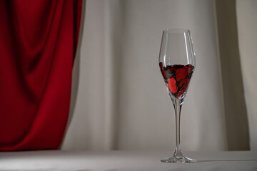 Wine glass with heart confetti on cream and red silk background. Minimalist lowkey holiday photo for Valentines